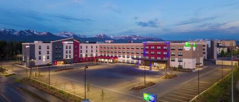 A hotel with a parking lot and a view of mountains in the background.