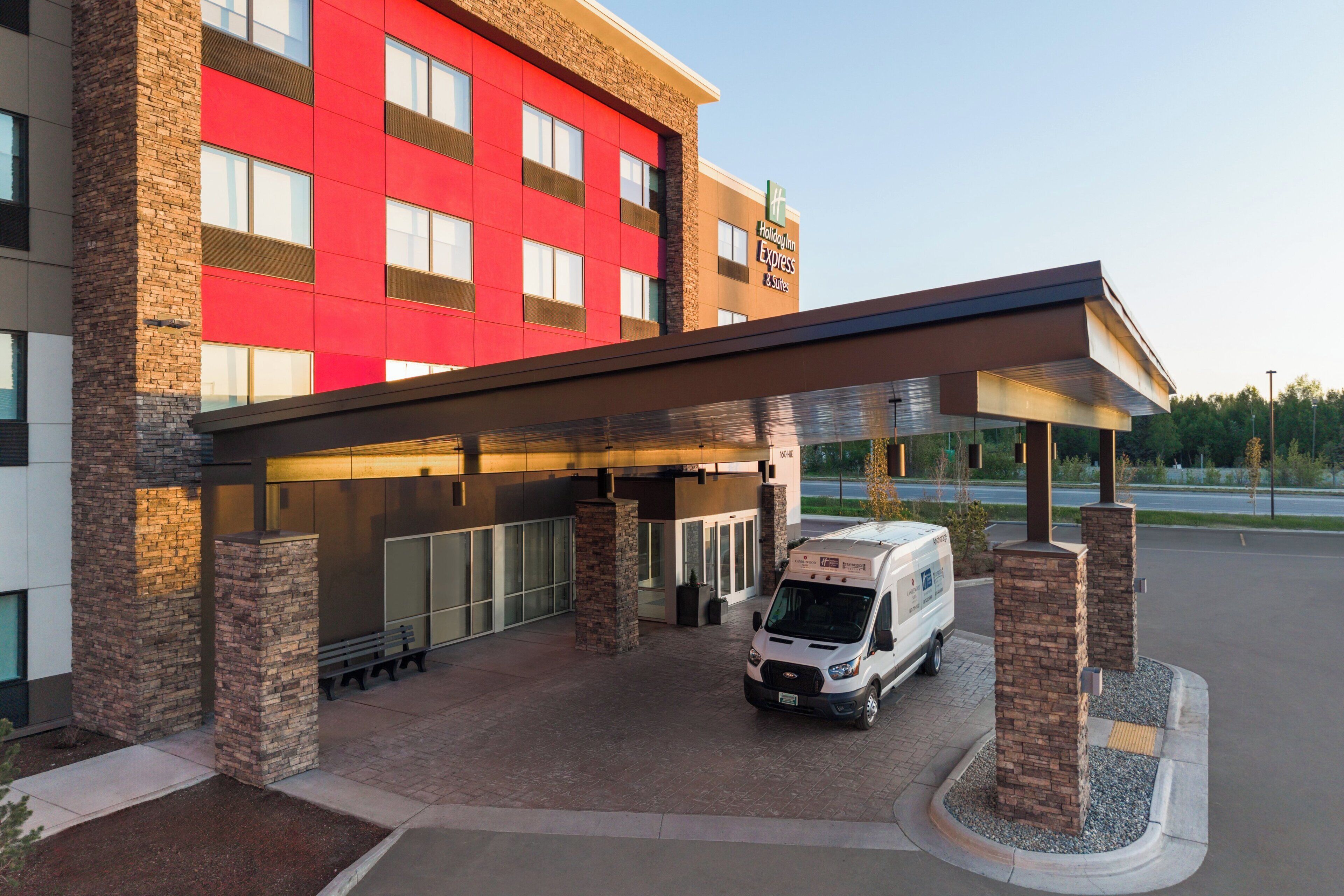A hotel with a red facade, a covered entrance, and a delivery van parked outside.