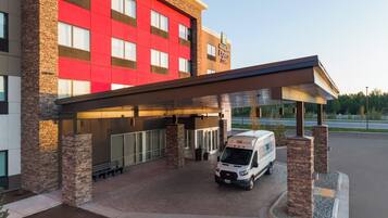A hotel with a red facade, a covered entrance, and a delivery van parked outside.