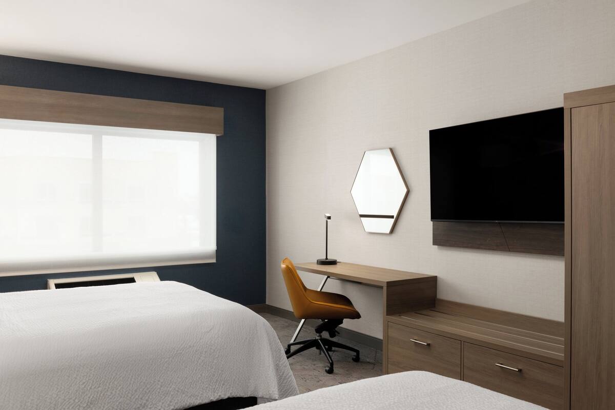 Une chambre d’hôtel avec deux lits, un bureau, une chaise, une télévision et une armoire.