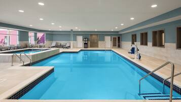 Una amplia piscina interior con agua cristalina, rodeada de sillones de descanso y una tumbona.