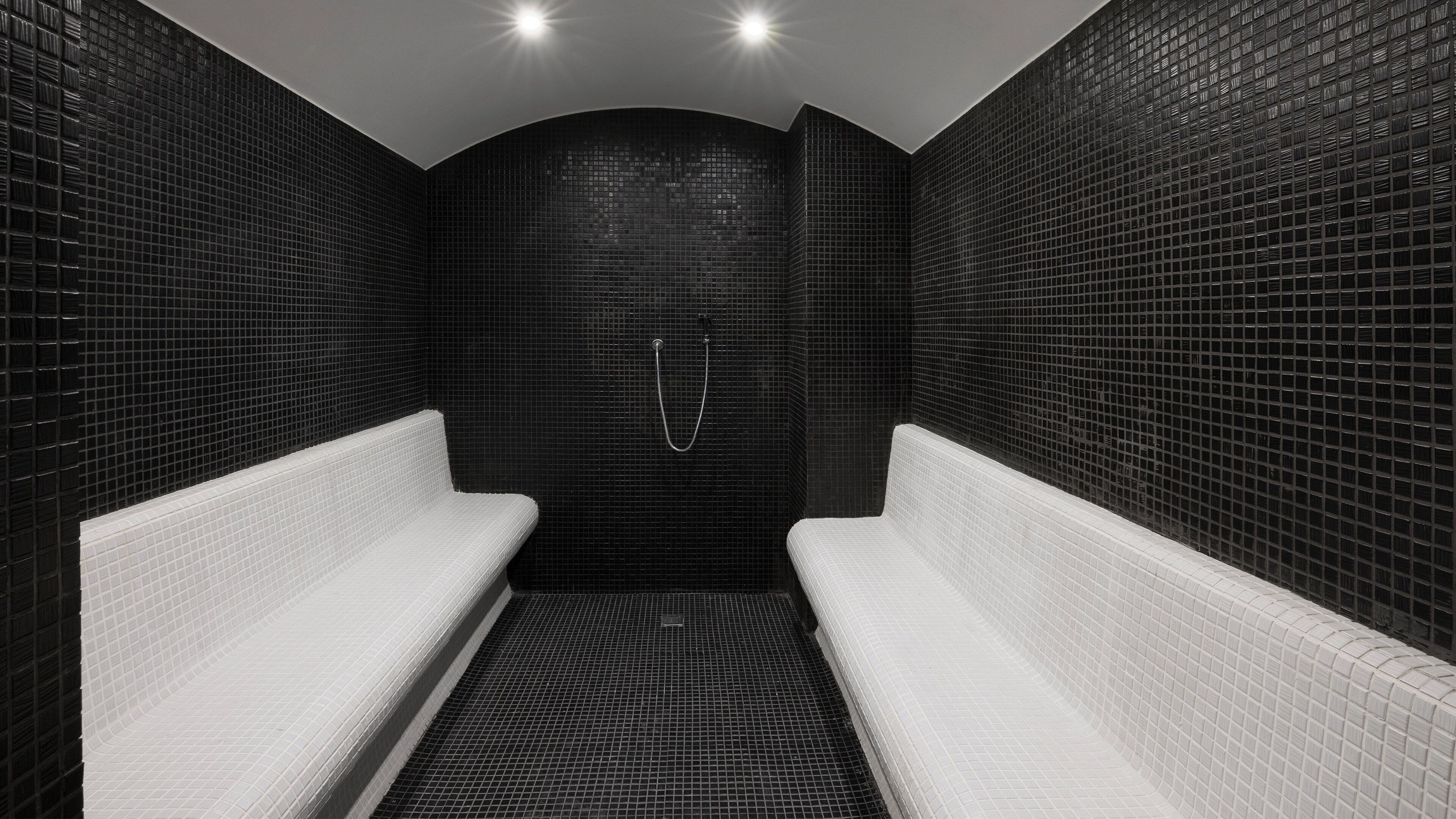 Un baño moderno con paredes de azulejos blanco y negro, una zona de ducha curva y dos bancos blancos.