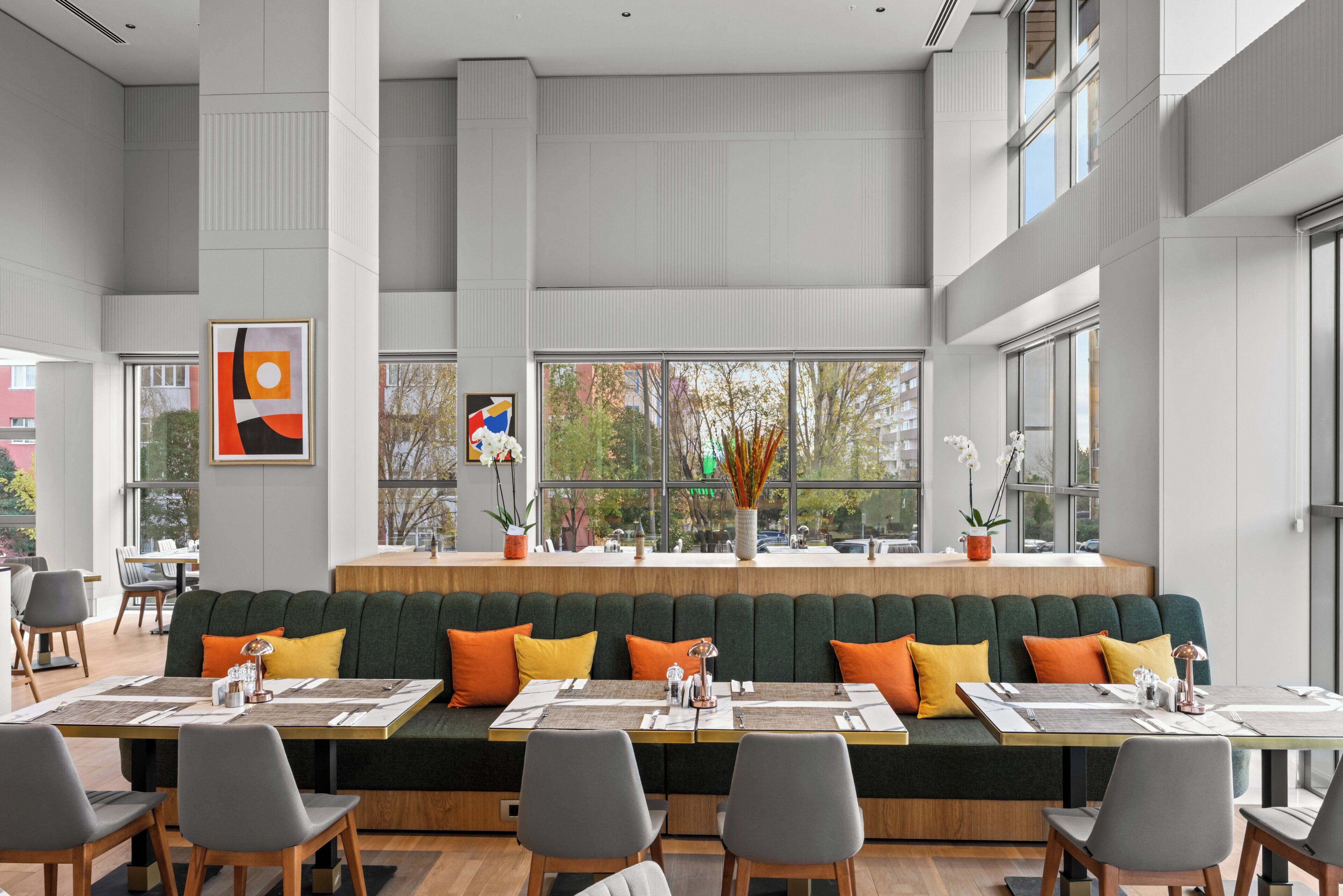 A modern dining area with a long green bench, multiple tables, and chairs.
