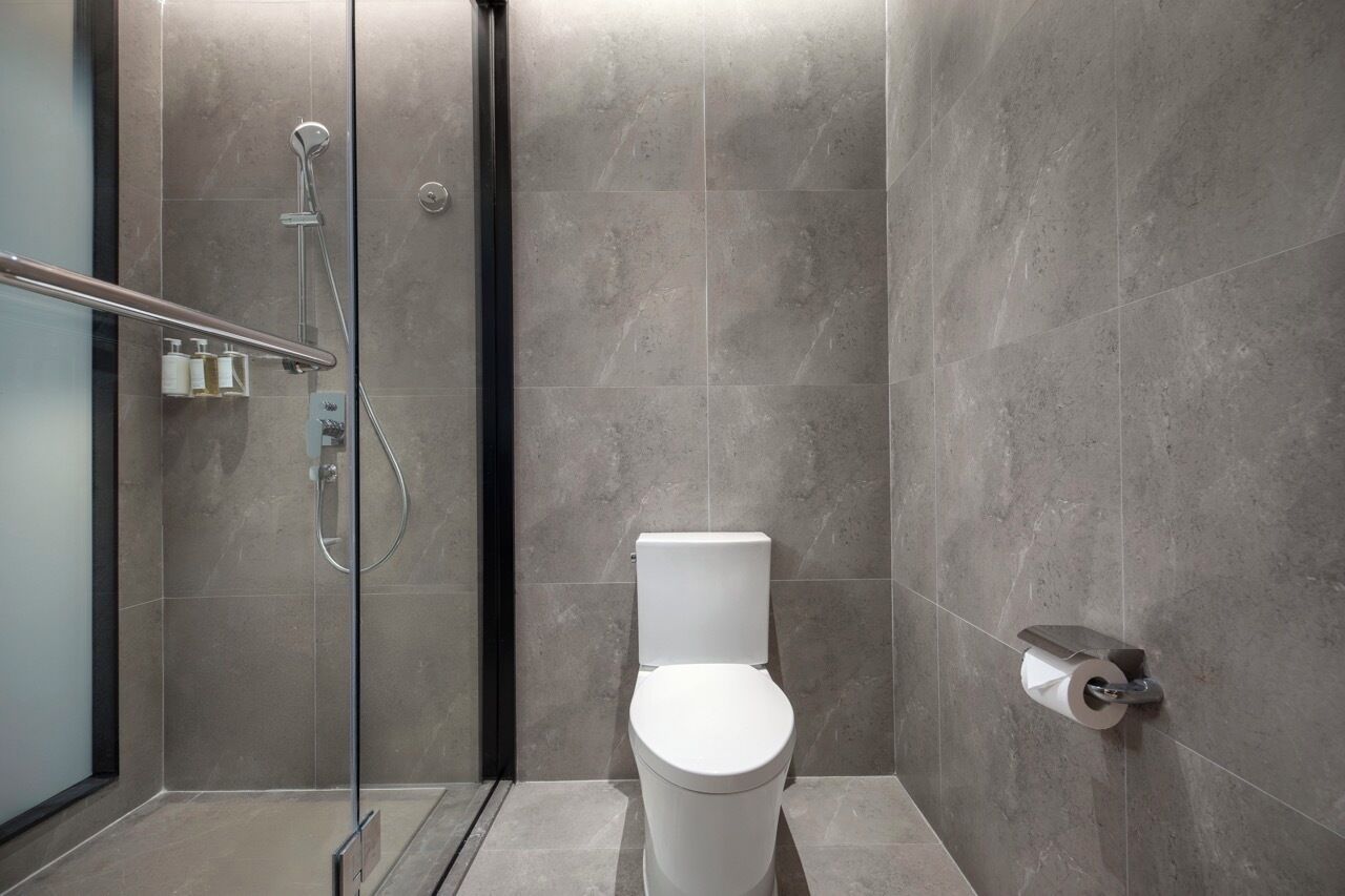 A modern bathroom with a glass-enclosed shower, a white toilet, and a toilet paper holder mounted on the wall.