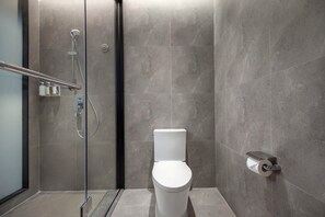 Un baño moderno con ducha envuelta en vidrio, un inodoro blanco y un dispensador de papel higiénico montado en la pared.