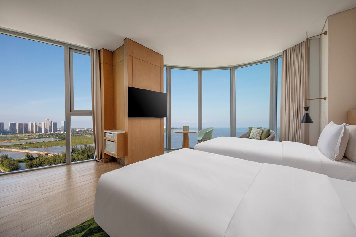 Habitación de hotel con dos camas, televisión, escritorio y vistas a la ciudad y al río.