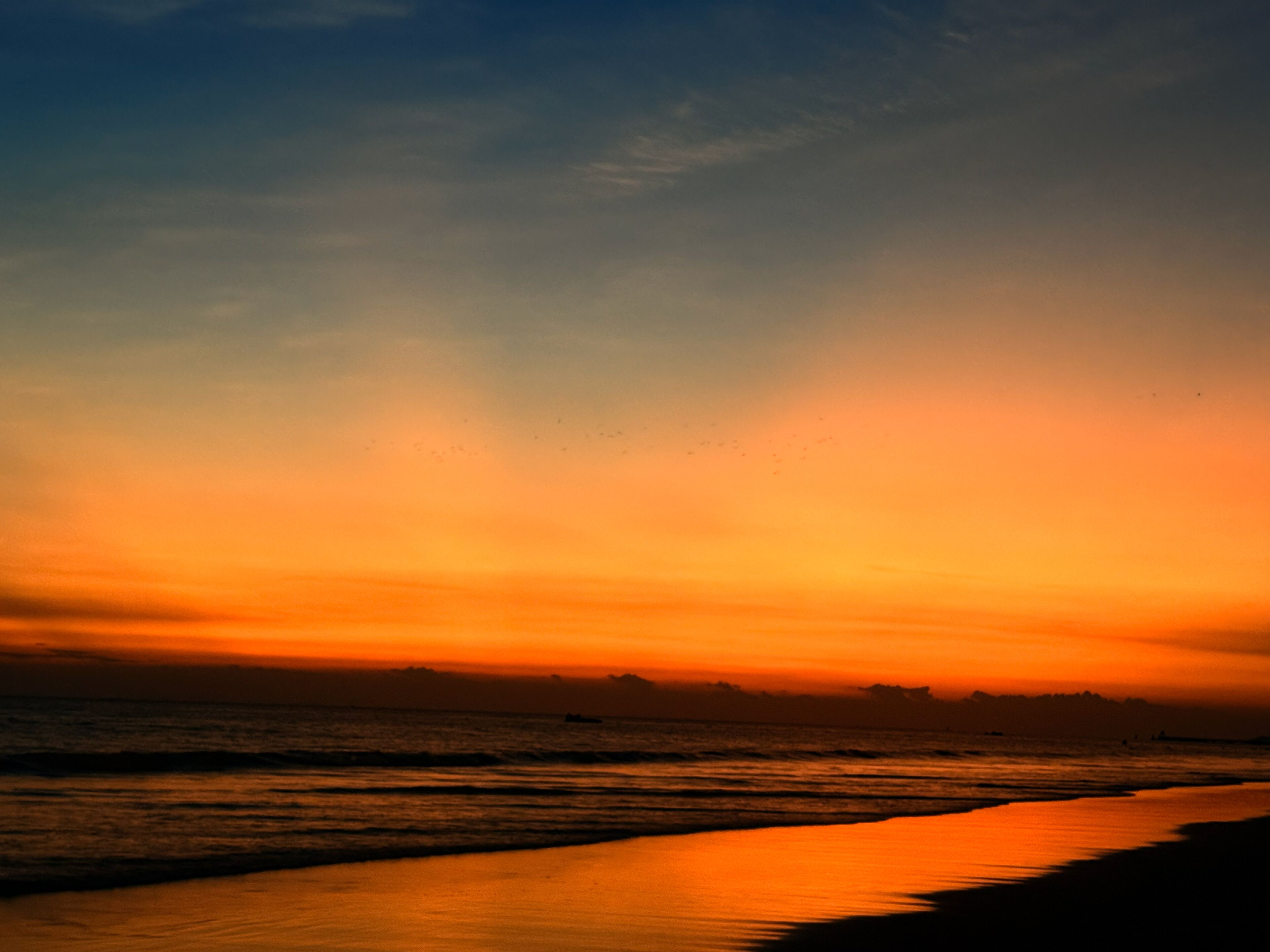 Ein Sonnenuntergang über einem Strand mit ruhigem Wasser, das den Himmel spiegelt.