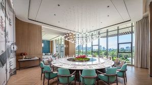 A modern dining area with a round table, teal chairs, and a city view through large windows.