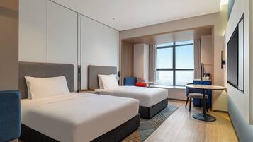 A hotel room with two beds, a desk, and a large window.