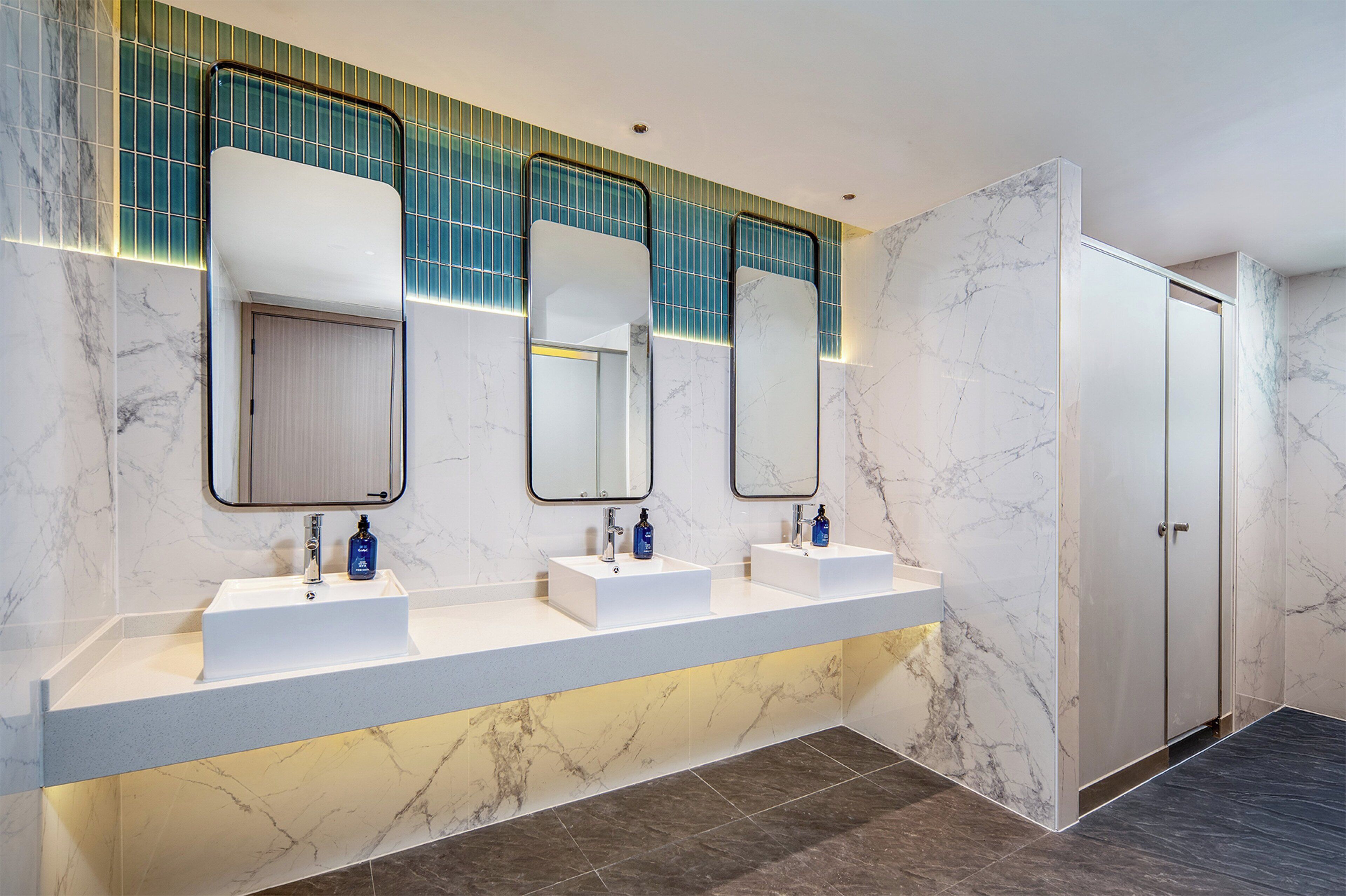 Un baño moderno con tres lavamanos, cada uno con un espejo encima, y un armario grande a la derecha.