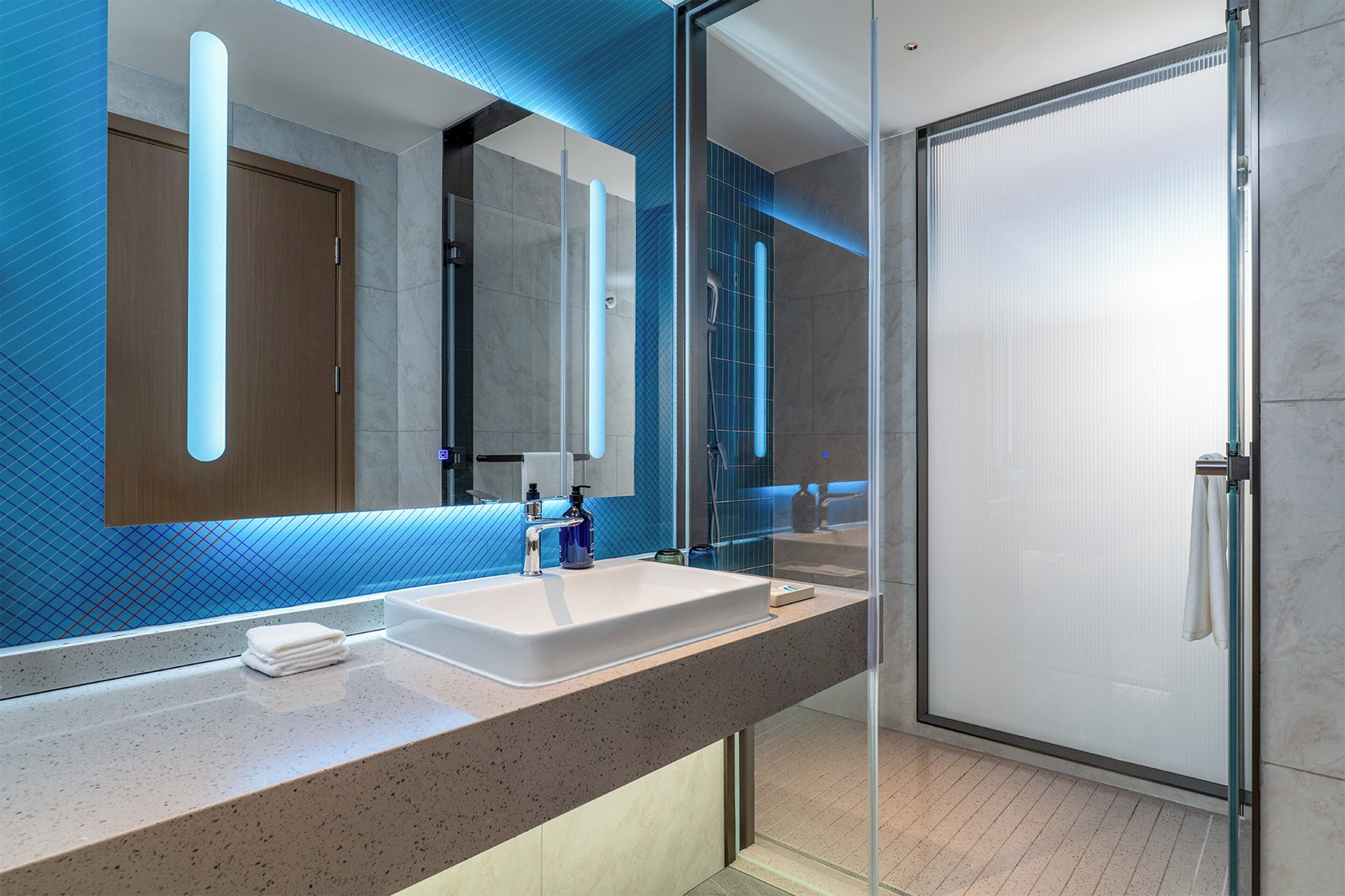 Une salle de bain moderne avec un grand miroir, un lavabo et une douche à parois de verre.