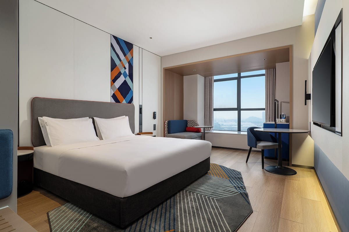 Ein modernes Hotelzimmer mit einem großen Bett, einem Schreibtisch und Blick auf die Stadt.