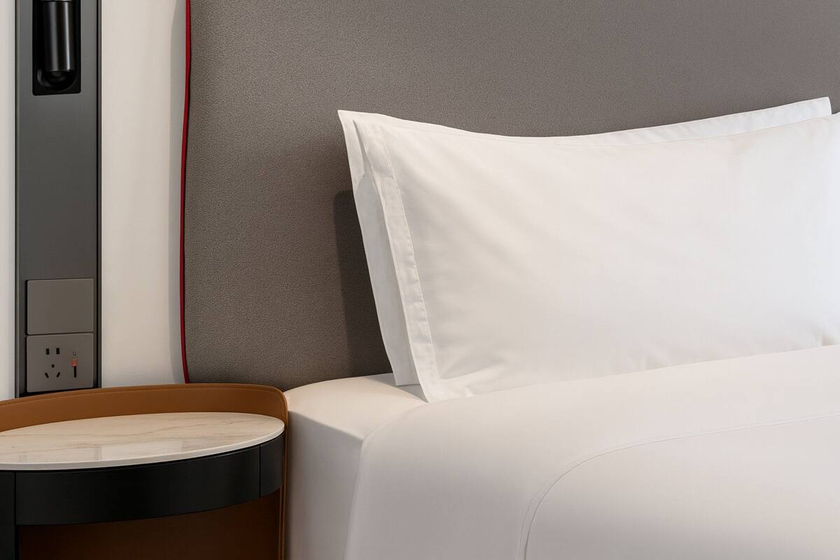 Ein ordentlich bezogenes Bett mit weißen Leinentüchern und einem grauen Kopfteil.