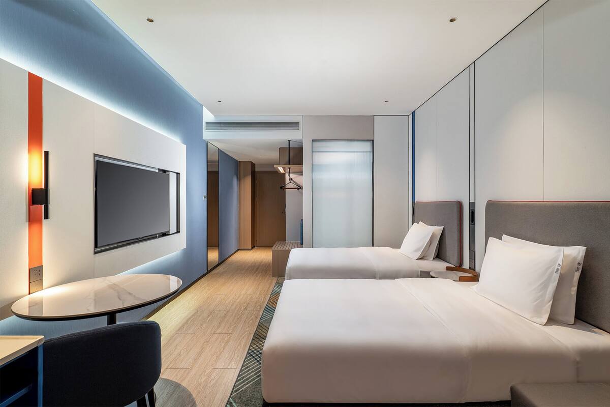 Ein modernes Hotelzimmer mit zwei Betten, einem Fernseher, einem kleinen Tisch und einer Sitzecke.