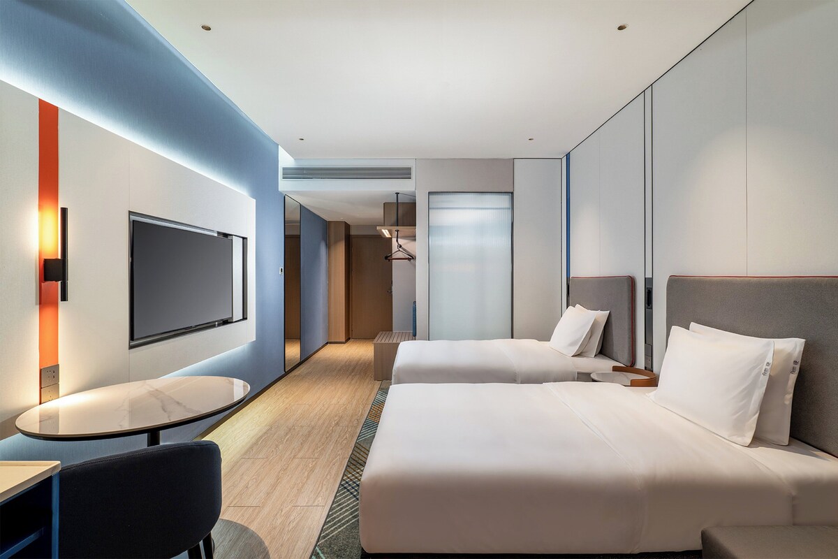 Ein modernes Hotelzimmer mit zwei Betten, einem Fernseher, einem kleinen Tisch und einer Sitzecke.
