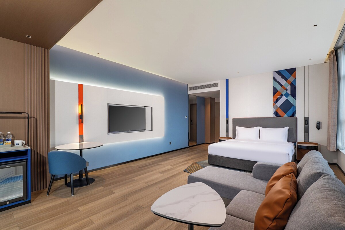 Ein modernes Hotelzimmer mit Bett, Sofa, Fernseher und einem kleinen Tisch.