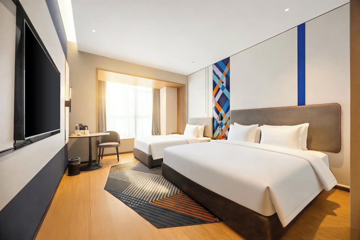 Ein Hotelzimmer mit zwei Betten, einem Schreibtisch, einem Stuhl, einem Fernseher und einem großen Fenster.