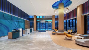 Un hall d’entrée moderne doté d’un comptoir de réception, d’un espace salon et de grandes fenêtres.