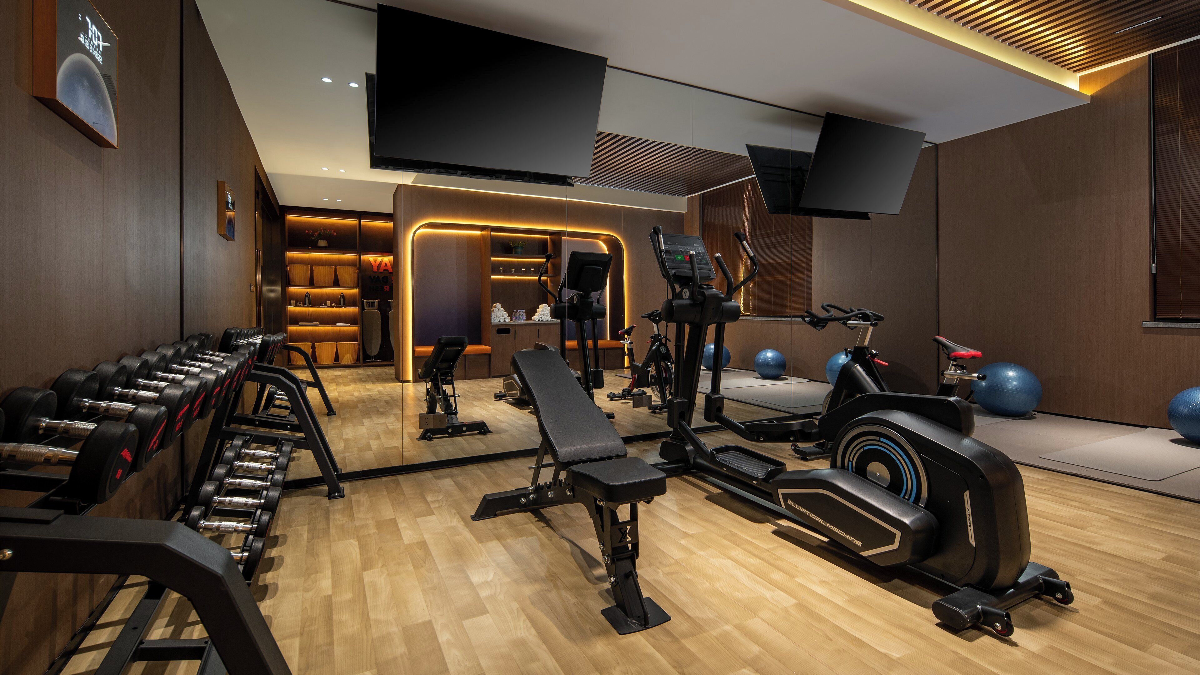 A modern gym with various exercise equipment, a bench, and a wall-mounted TV.