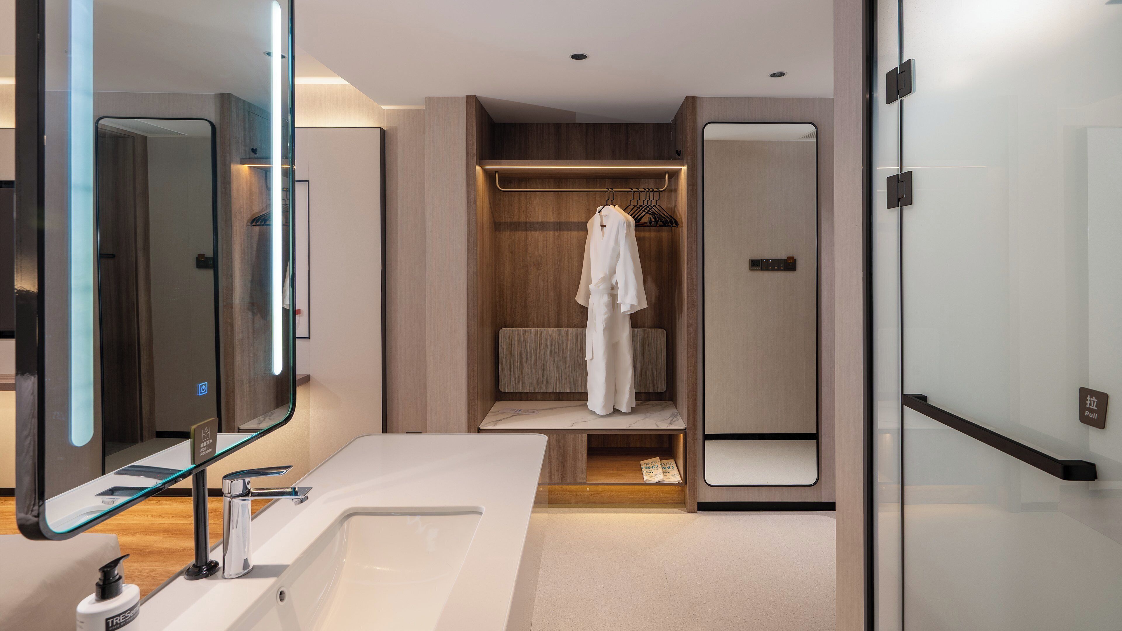 A modern bathroom with a large mirror, a white sink, and a wooden vanity.