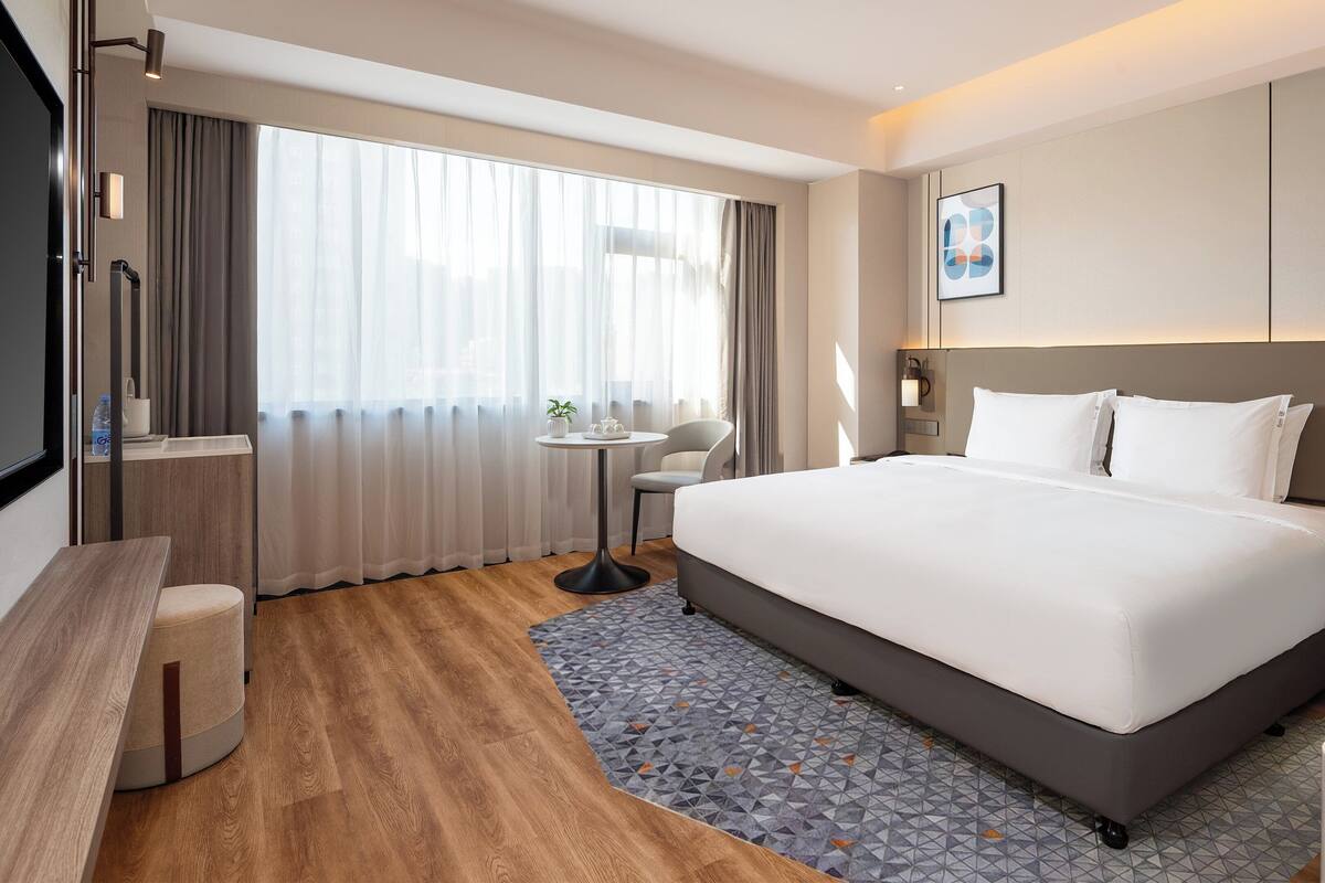 Une chambre d’hôtel moderne équipée d’un grand lit, d’un bureau, d’une chaise, d’une petite table avec une plante et d’un téléviseur.