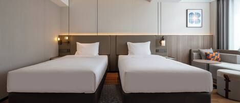 A hotel room with two beds, a sofa, a small table, and a wall-mounted light fixture.