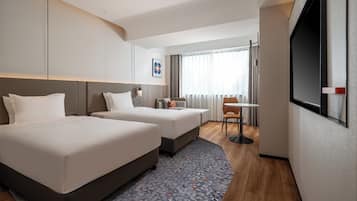 Habitación de hotel con dos camas, una mesita, televisión y ventana con cortinas.