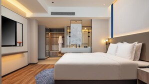 Une chambre d’hôtel moderne dotée d’un grand lit, d’un téléviseur intégré, d’une coiffeuse avec miroir et d’un dressing.