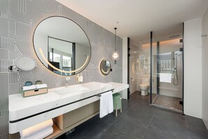 A modern bathroom with a large mirror, two sinks, a toilet, and a glass-enclosed shower.