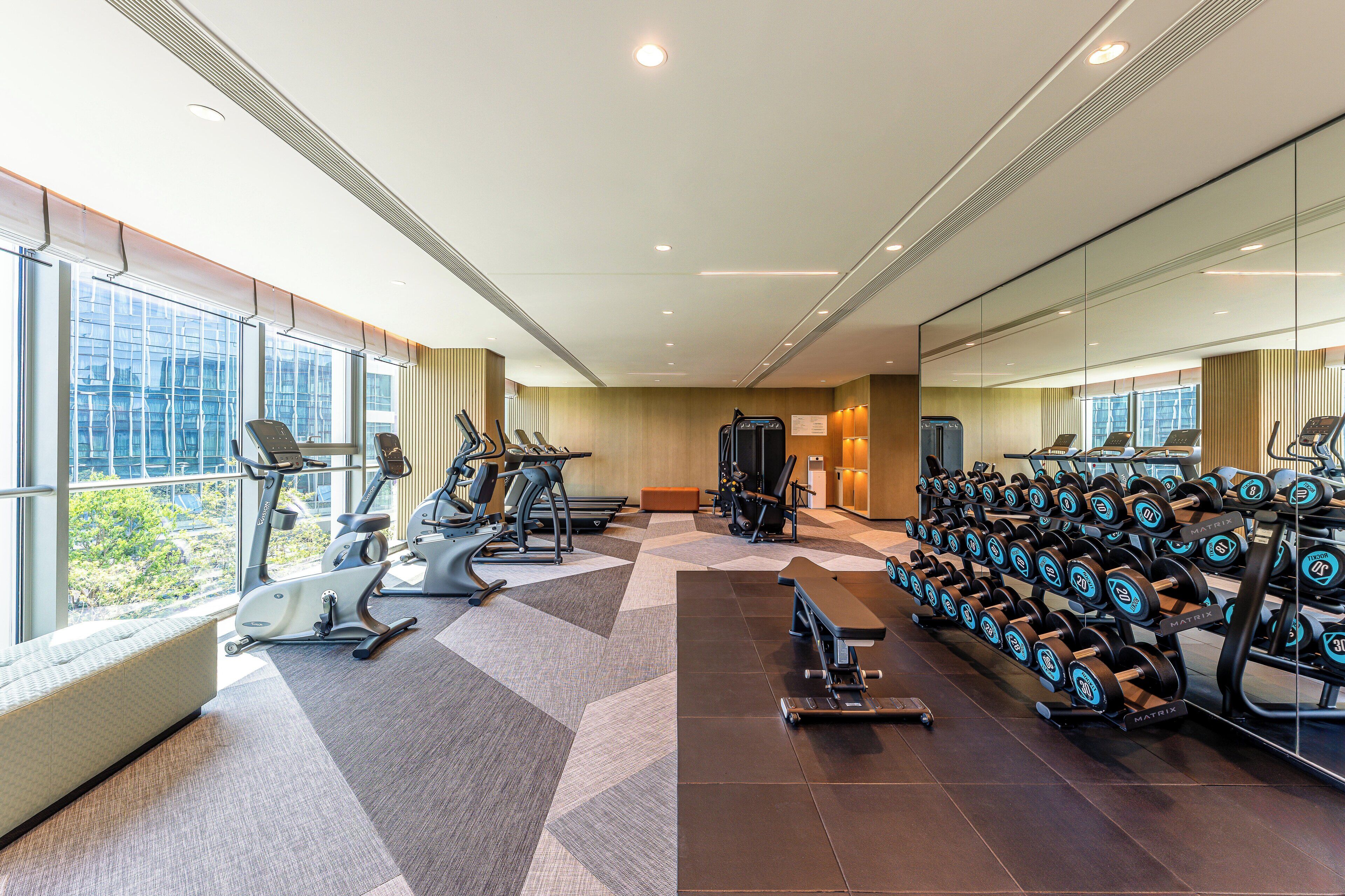 Un gimnasio moderno con máquinas de cardio, estaciones de pesas y una amplia pared de espejos.