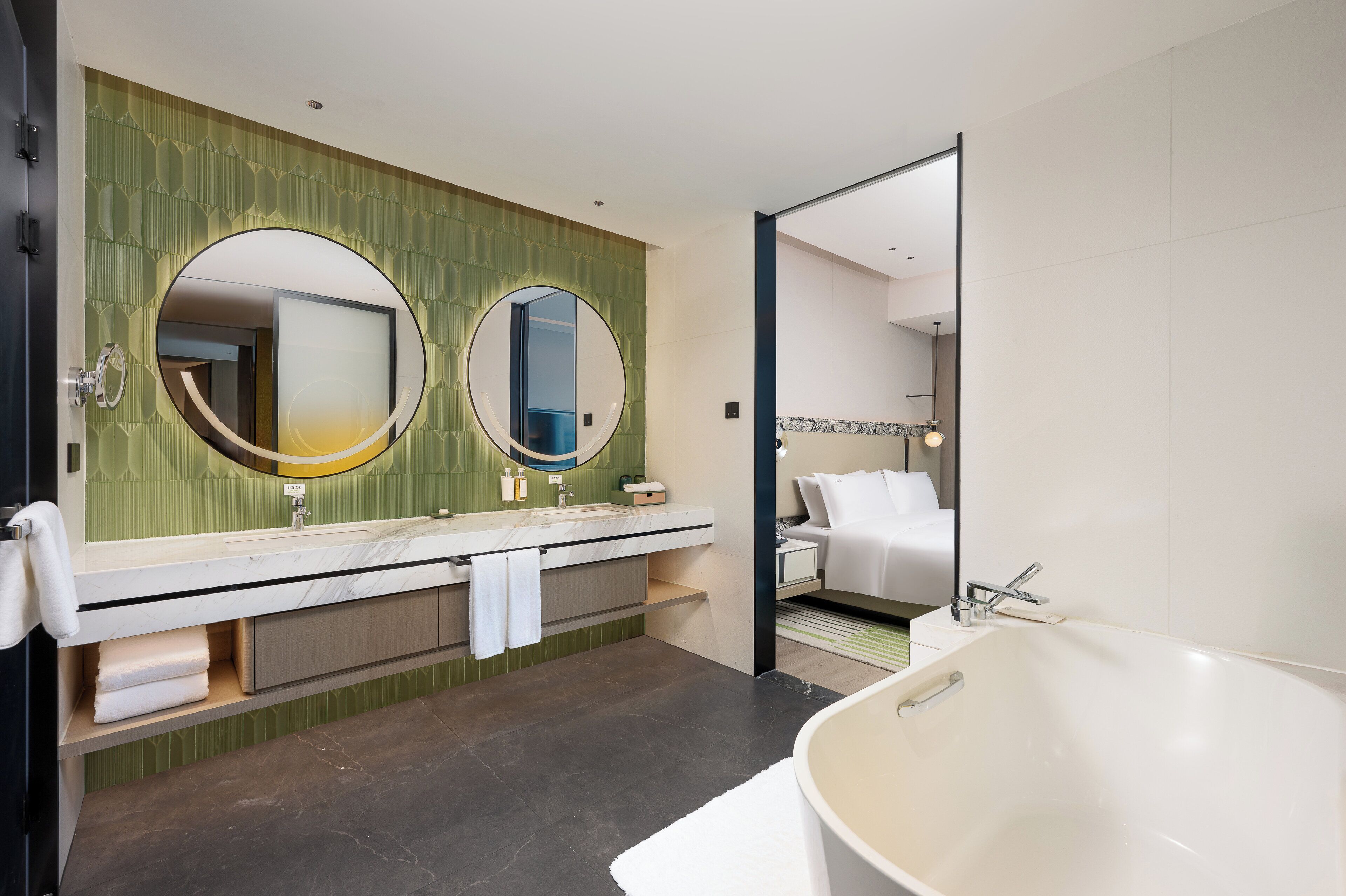 A modern bathroom with a large bathtub, two sinks with mirrors, and a green patterned wall.