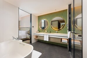 A modern bathroom with a freestanding bathtub, a double vanity with two round mirrors, and a green patterned wall.