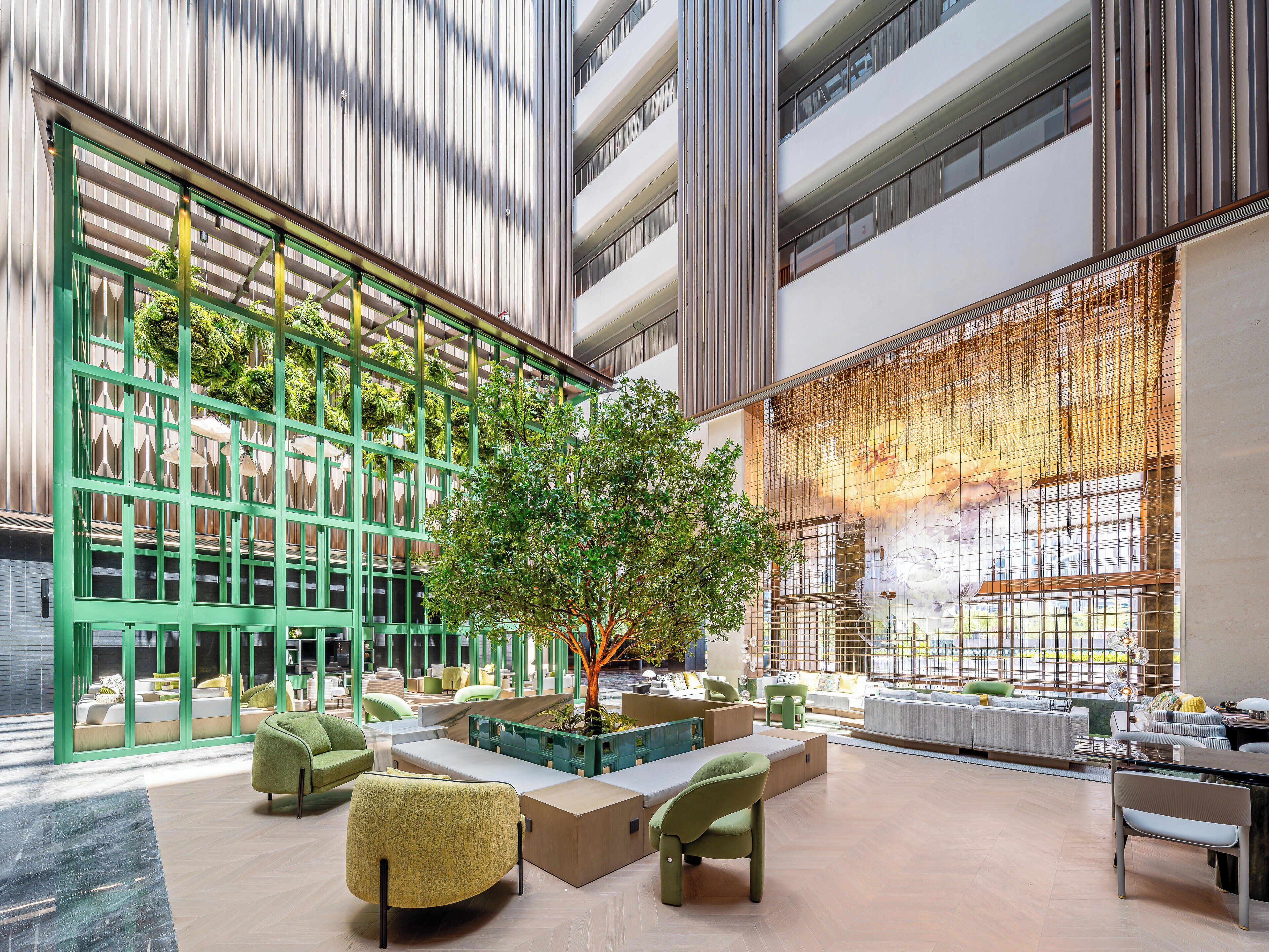 A modern indoor space with seating areas, a central tree, and a large window with a decorative screen.