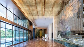 Un vestíbulo amplio con techo alto, ventanas grandes y un piso de mármol que refleja la luz.