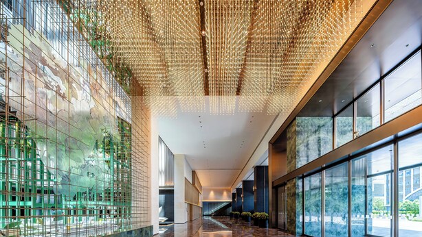 Un hall espacioso con suelo de mármol reflectante, amplias ventanas con vistas al exterior y un techo decorado con lámparas colgantes.