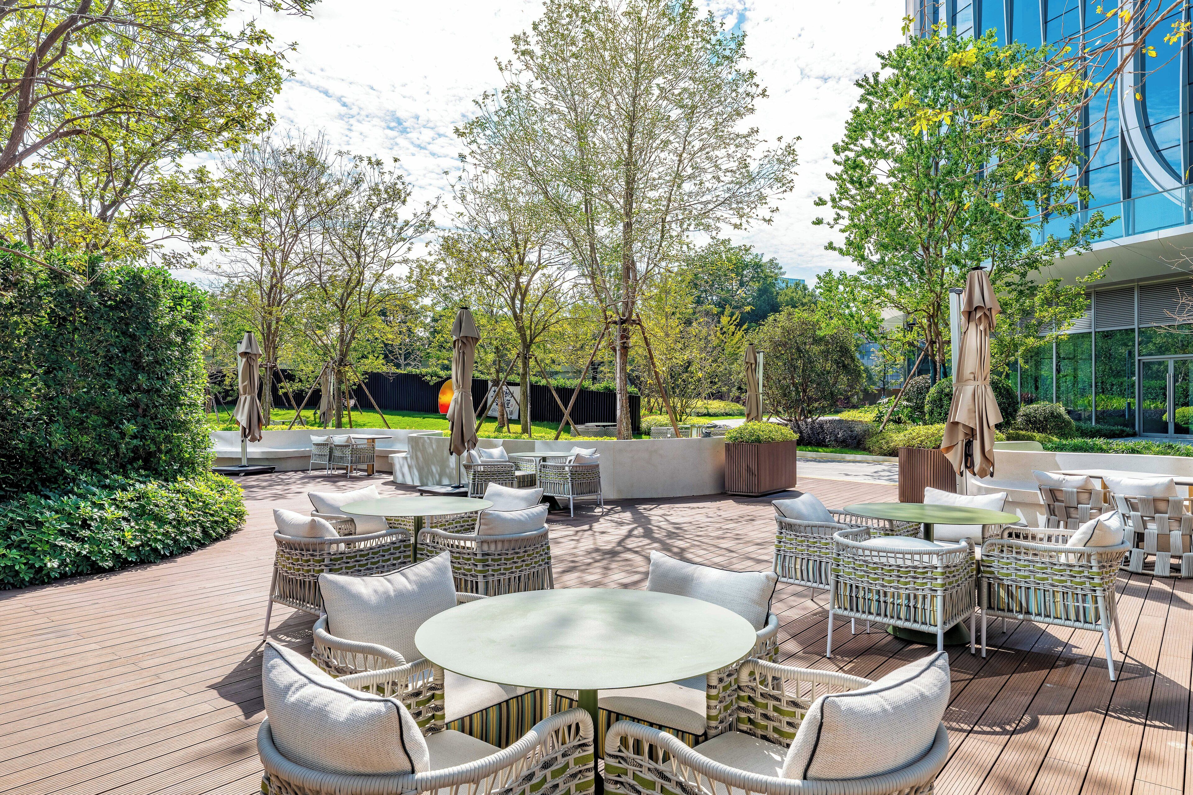 An outdoor patio with wicker furniture, umbrellas, and a view of a modern building.