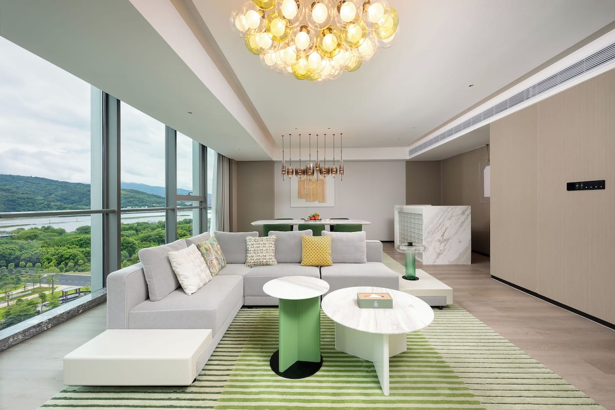 Ein modernes Wohnzimmer mit einem großen Sofa, zwei Couchtischen und Blick auf einen Fluss und Grünflächen.