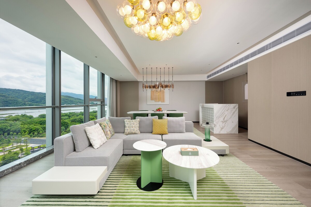 Una sala moderna con un sofá grande, dos mesas auxiliares y vistas a un río y vegetación.