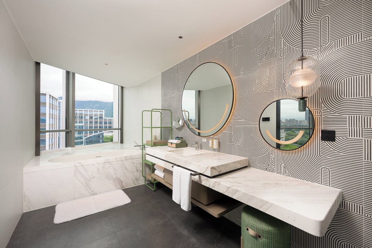 Un baño moderno con un ventanal grande, un lavabo de mármol y un papel tapiz decorativo.