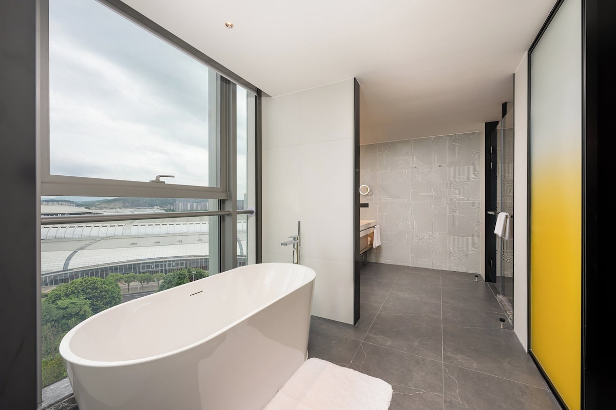 Ein modernes Badezimmer mit einer freistehenden Badewanne, einem großen Fenster und Blick auf die Stadt.