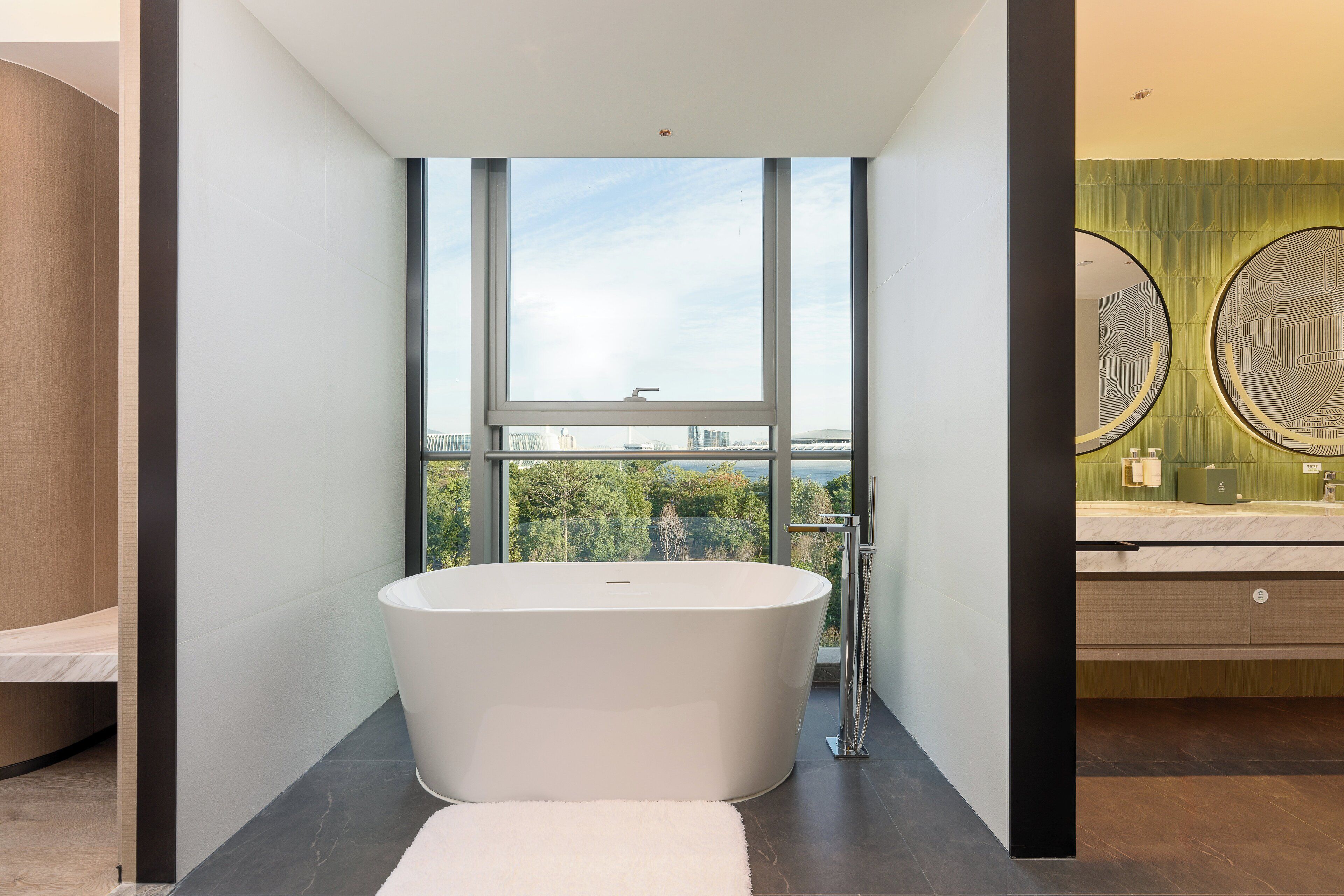 A modern bathroom with a freestanding bathtub, a large window, and a view of the city.
