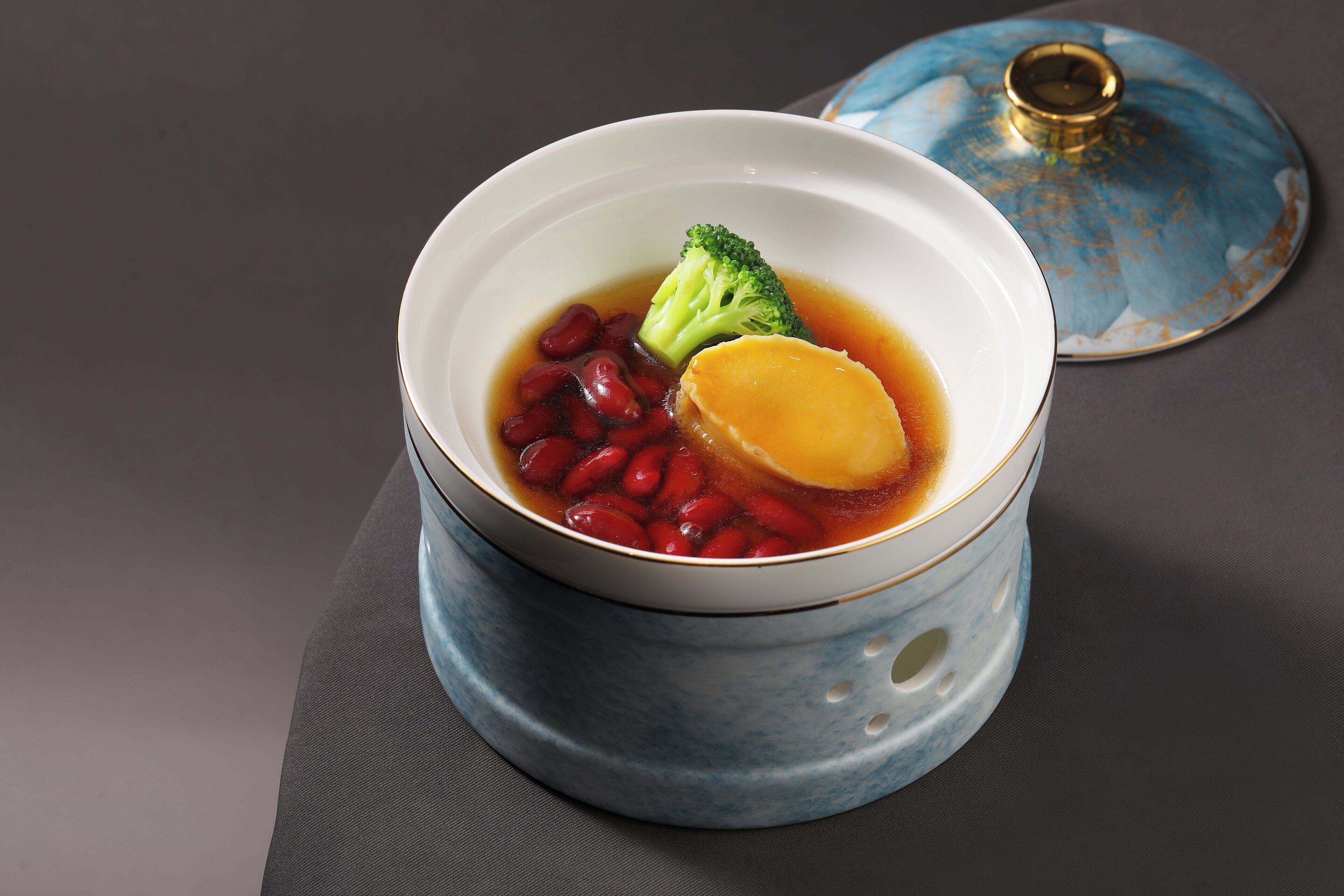 Un tazón de sopa con verduras y frijoles, sobre una mesa con una tapa azul al fondo.