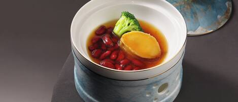 Un tazón de sopa con verduras y frijoles, sobre una mesa con una tapa azul al fondo.