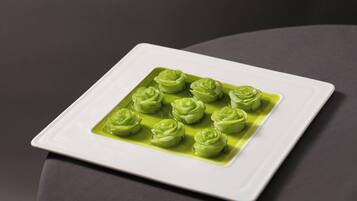 A white square plate with green rose-shaped food items on a dark surface.
