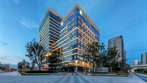 A modern hotel with a prominent 'Holiday Inn Express' sign, featuring a multi-story structure with a glass facade and a landscaped entrance area. - Holiday Inn Express Taizhou Jiaojiang by IHG (Taizhou)
