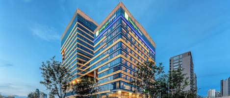 A modern hotel with a prominent 'Holiday Inn Express' sign, featuring a multi-story structure with a glass facade and a landscaped entrance area.