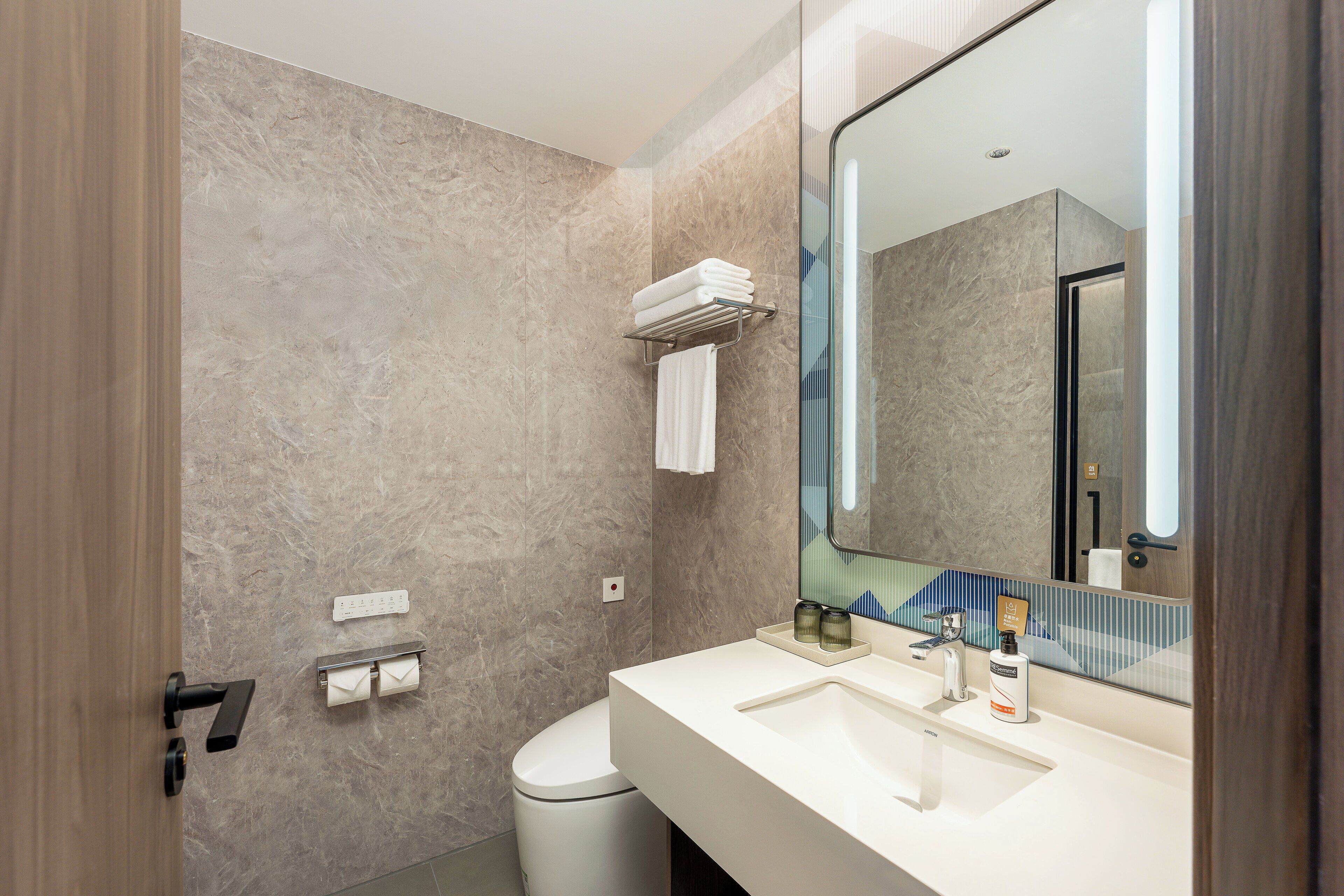 Un baño moderno con pared de mármol, un lavamanos blanco, un espejo grande y un perchero para toallas.