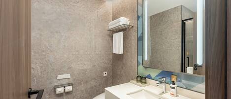 Un baño moderno con pared de mármol, un lavamanos blanco, un espejo grande y un perchero para toallas.
