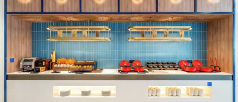 A modern kitchen with blue tiles, wooden cabinets, and a coffee station.