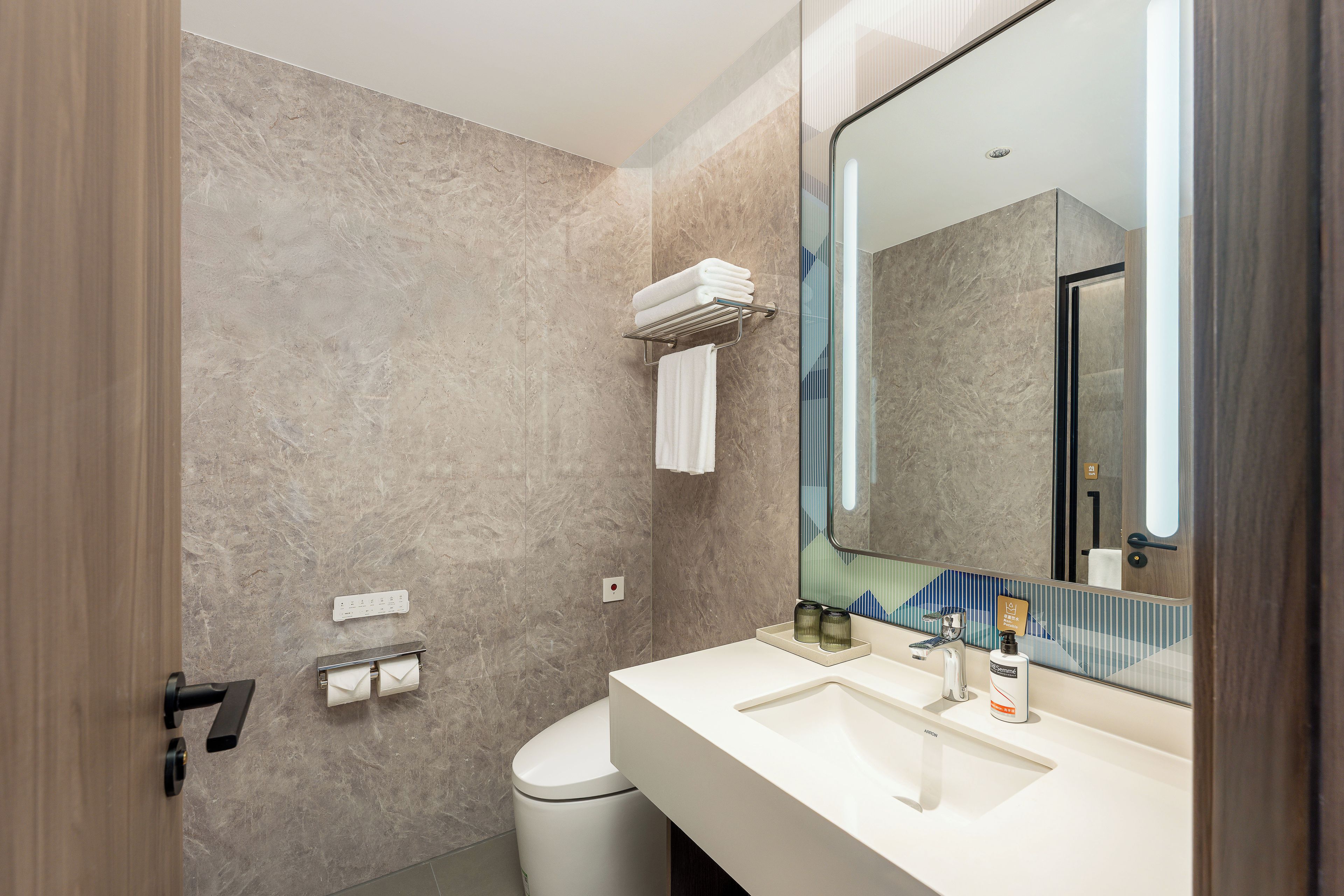 A modern bathroom with a marble wall, a white sink, a large mirror, and a towel rack.
